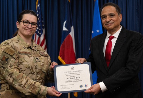 A person in military uniform and a person in a suit both face the camera holding a certificate