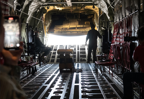 Two military personnel standing in the open rear of a military transport aircraft in-flight