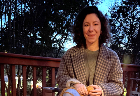 A woman wearing a plaid flannel shirt sitting on an outdoor patio surrounded by trees